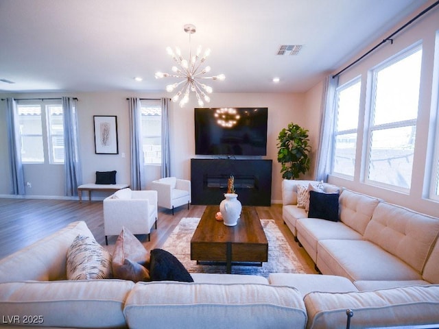 living area with visible vents, light wood-style flooring, recessed lighting, a glass covered fireplace, and a chandelier