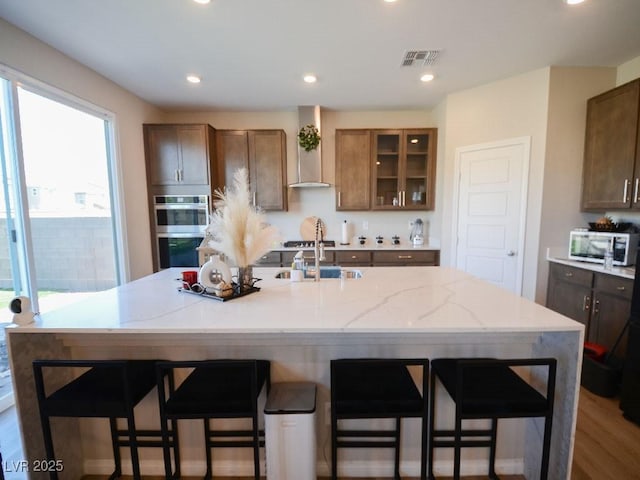 kitchen with a kitchen breakfast bar, wall chimney exhaust hood, visible vents, and appliances with stainless steel finishes