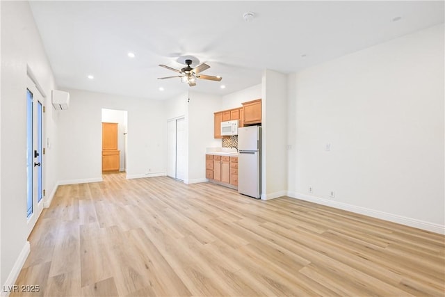 unfurnished living room featuring light wood-style flooring, ceiling fan, baseboards, and a wall unit AC