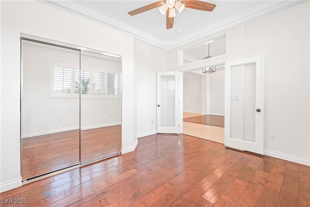 unfurnished bedroom with a closet, baseboards, hardwood / wood-style flooring, and ceiling fan with notable chandelier