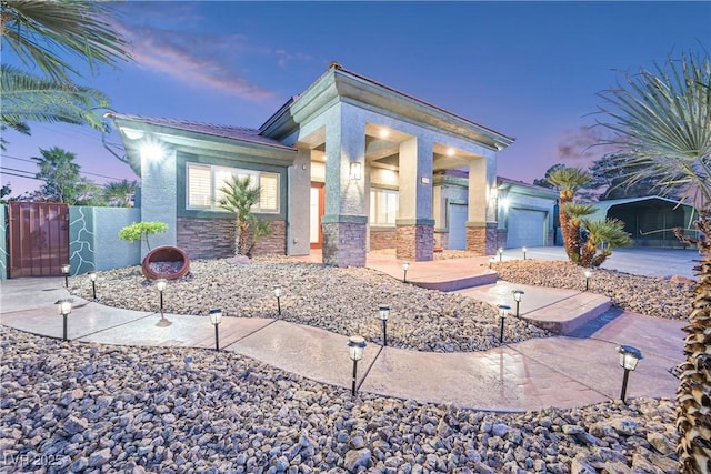view of front facade featuring a garage, fence, stone siding, and stucco siding