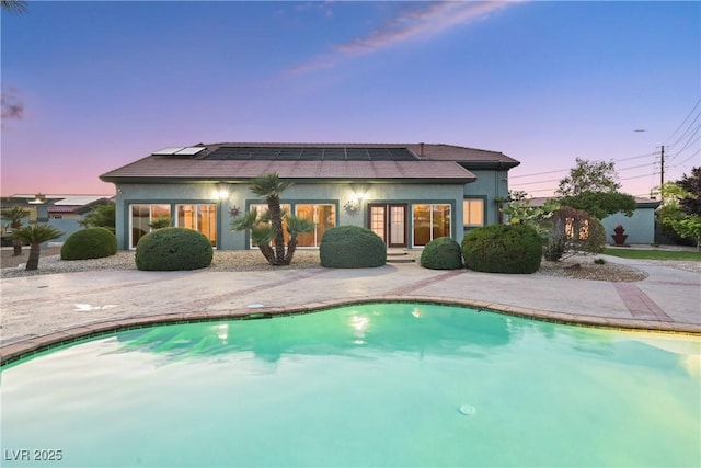 rear view of house with an outdoor pool, a patio, stucco siding, and solar panels