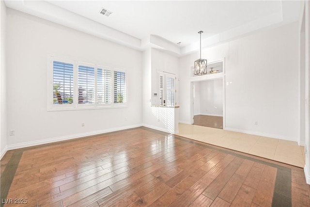 empty room featuring a notable chandelier, baseboards, visible vents, a raised ceiling, and wood-type flooring