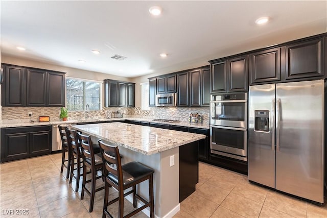 kitchen with light tile patterned floors, a kitchen island, a sink, stainless steel appliances, and backsplash