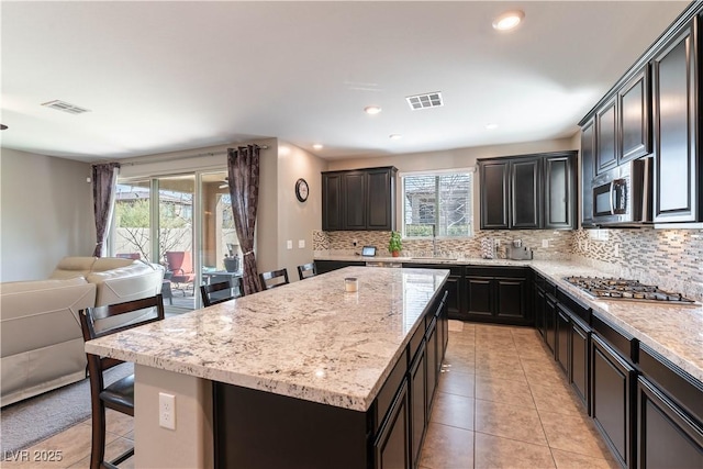 kitchen with visible vents, backsplash, a center island, light stone countertops, and appliances with stainless steel finishes