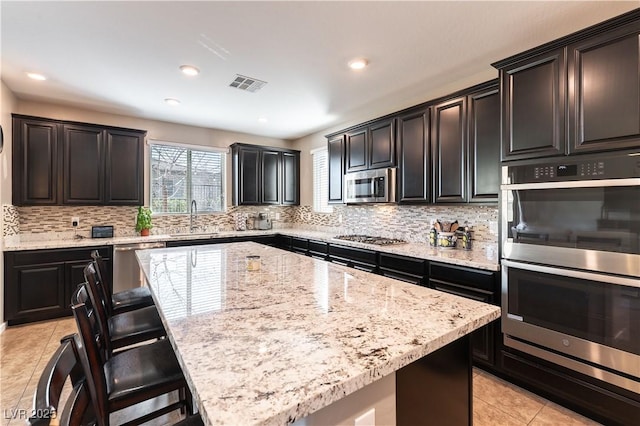 kitchen with visible vents, a breakfast bar, a sink, stainless steel appliances, and light tile patterned floors