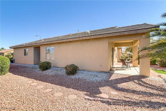 back of property featuring a patio, roof with shingles, and stucco siding