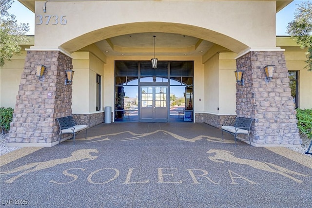 entrance to property featuring stone siding, stucco siding, and french doors