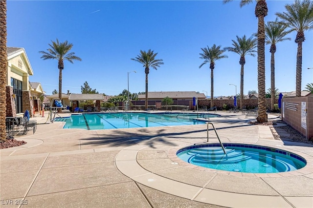 pool with a patio area, a community hot tub, and fence