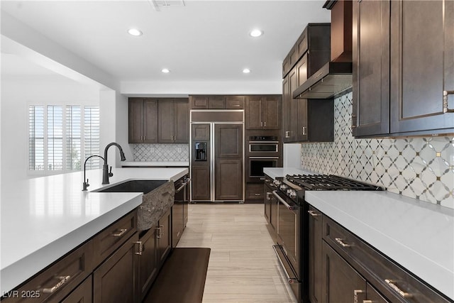 kitchen with premium appliances, dark brown cabinetry, light countertops, and wall chimney range hood