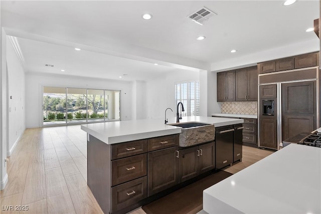 kitchen featuring visible vents, a center island with sink, a sink, backsplash, and light countertops