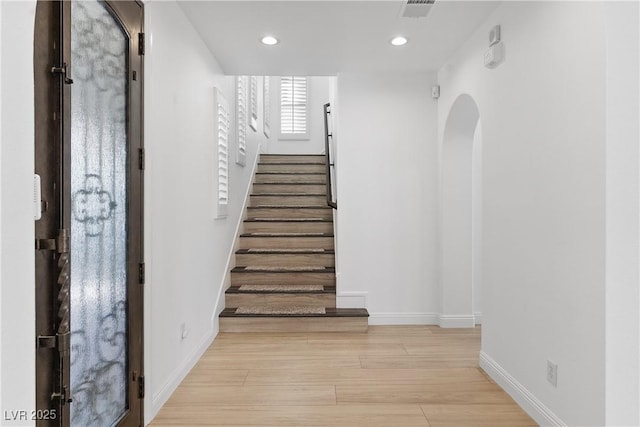 staircase featuring visible vents, baseboards, recessed lighting, wood finished floors, and arched walkways