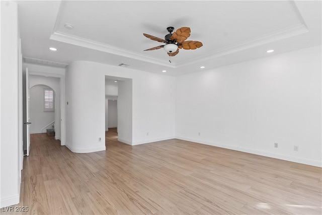 unfurnished room featuring visible vents, arched walkways, crown molding, light wood finished floors, and a raised ceiling