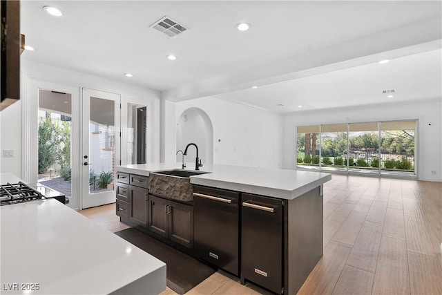 kitchen featuring visible vents, a kitchen island with sink, a sink, light countertops, and open floor plan