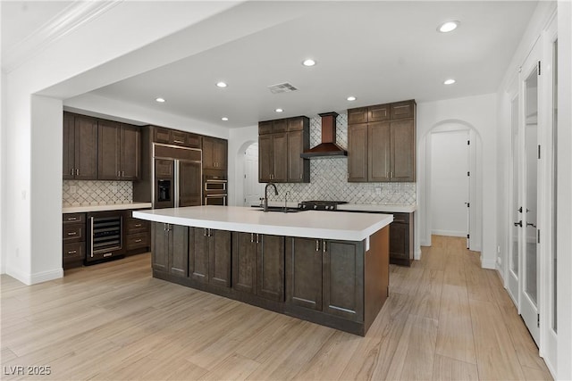 kitchen featuring paneled built in fridge, wall chimney exhaust hood, beverage cooler, and arched walkways