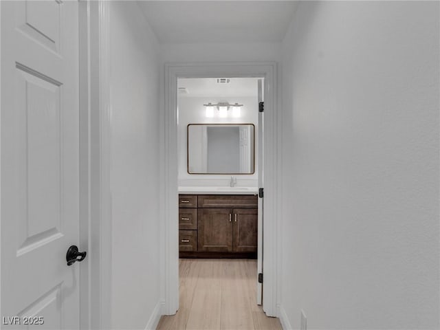 hall featuring a sink, light wood-type flooring, and baseboards