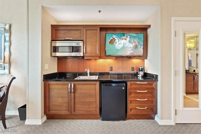 kitchen with brown cabinetry, stainless steel microwave, dark countertops, and a sink