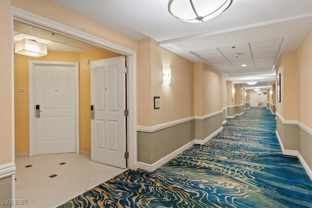 hallway with tile patterned floors, a paneled ceiling, and baseboards