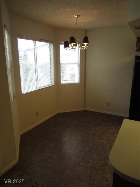 unfurnished dining area featuring a notable chandelier, a textured ceiling, and baseboards