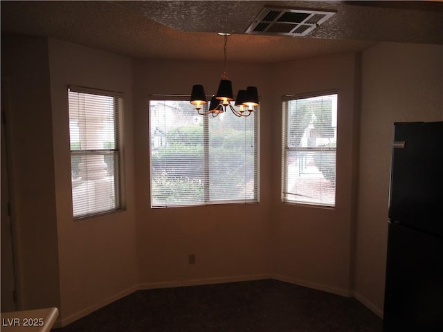 unfurnished dining area with an inviting chandelier, baseboards, visible vents, and a textured ceiling