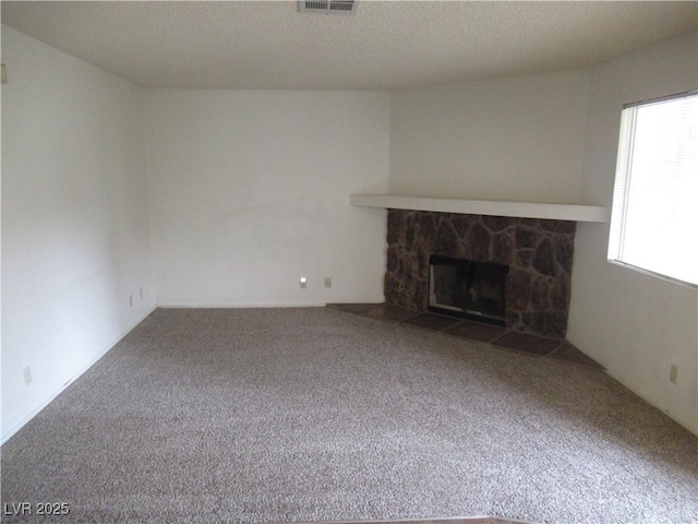 unfurnished living room featuring a stone fireplace, a textured ceiling, visible vents, and carpet floors