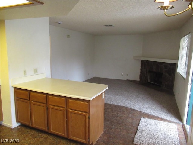 kitchen with visible vents, brown cabinets, open floor plan, a stone fireplace, and a peninsula