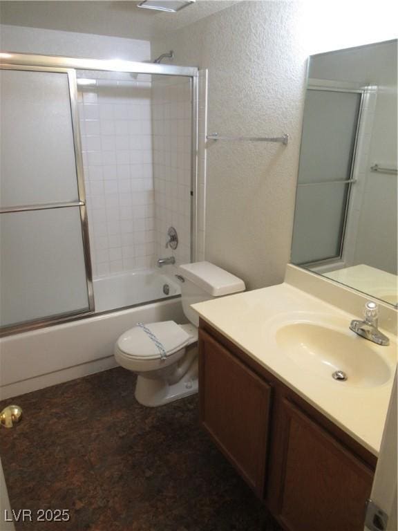 full bath featuring vanity, toilet, a textured wall, and combined bath / shower with glass door