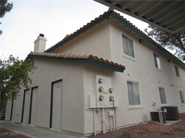 view of home's exterior featuring central air condition unit, stucco siding, a tiled roof, and a chimney