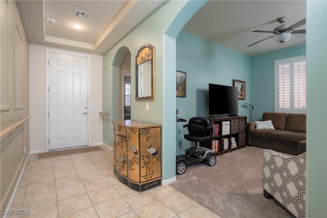 foyer entrance with visible vents, light carpet, arched walkways, light tile patterned flooring, and a raised ceiling