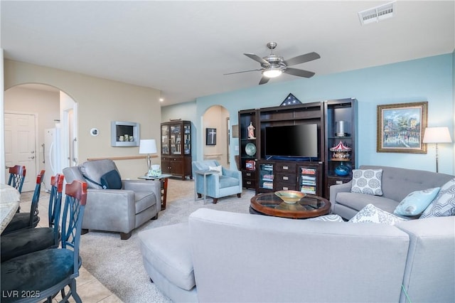 living area featuring light tile patterned floors, a ceiling fan, visible vents, arched walkways, and light carpet