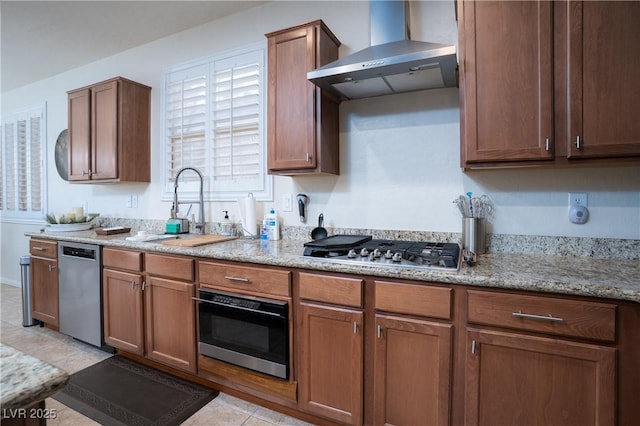 kitchen featuring light stone counters, light tile patterned floors, a sink, appliances with stainless steel finishes, and wall chimney range hood