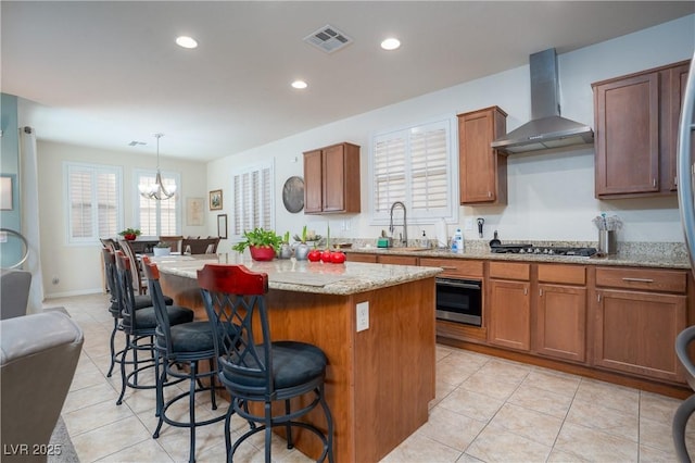 kitchen featuring a kitchen bar, visible vents, a kitchen island, wall chimney range hood, and stainless steel gas cooktop