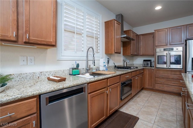 kitchen featuring light stone countertops, light tile patterned floors, appliances with stainless steel finishes, wall chimney exhaust hood, and a sink