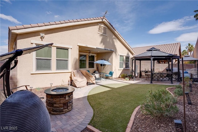 back of property with a gazebo, stucco siding, and a fire pit