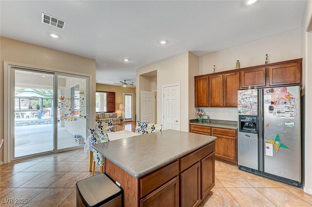 kitchen with visible vents, stainless steel fridge, a kitchen island, and brown cabinets