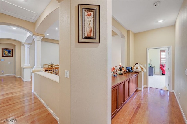 hall with light wood finished floors, baseboards, decorative columns, recessed lighting, and arched walkways