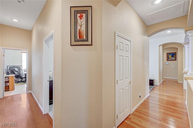 hall featuring decorative columns, light wood-style floors, arched walkways, and baseboards