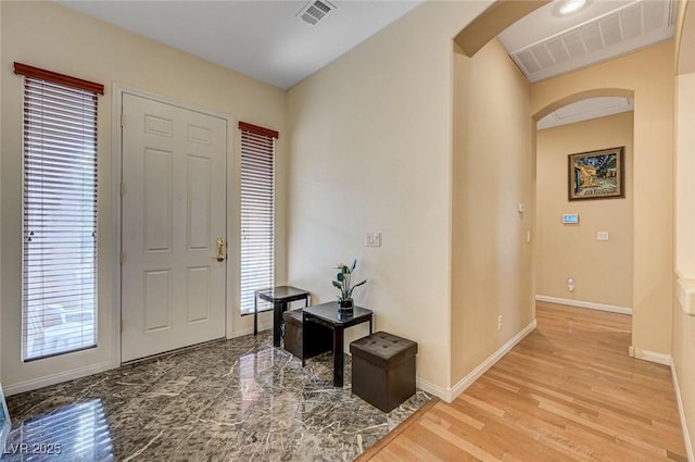 foyer featuring wood finished floors, plenty of natural light, arched walkways, and visible vents