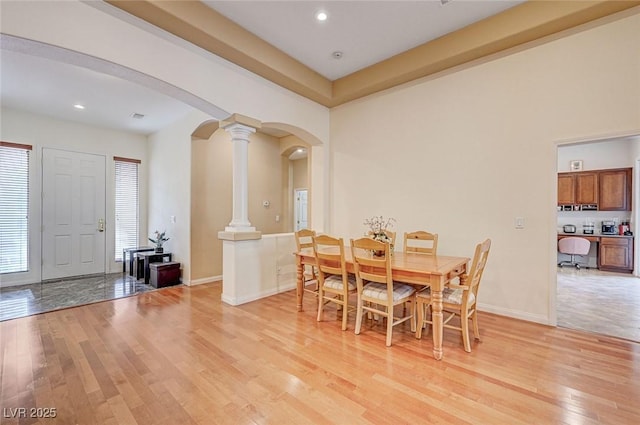 dining room with decorative columns, arched walkways, light wood-style floors, and baseboards