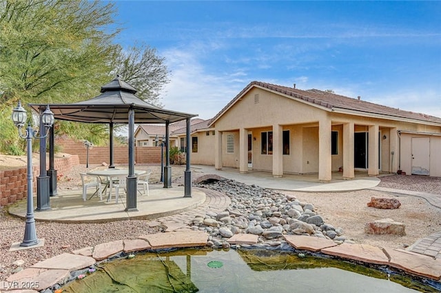 rear view of property featuring a gazebo, a patio, fence, and stucco siding