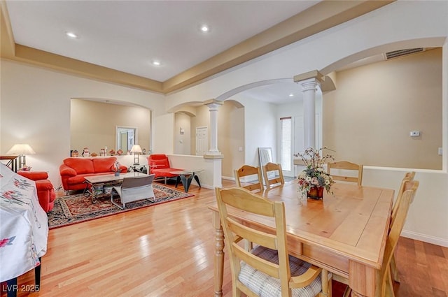 dining room featuring visible vents, wood finished floors, arched walkways, baseboards, and ornate columns