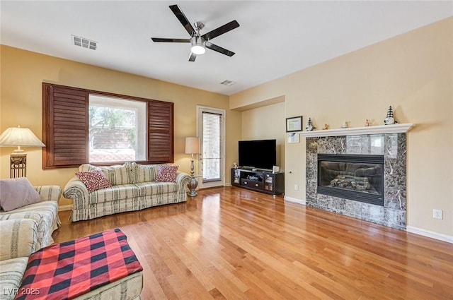 living area with visible vents, a ceiling fan, wood finished floors, and a high end fireplace