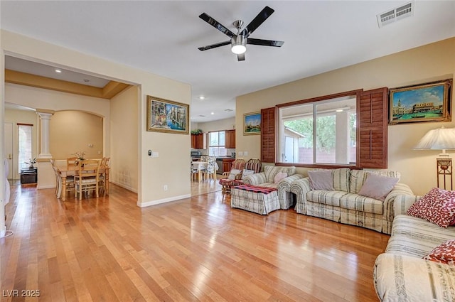 living room with decorative columns, visible vents, light wood-type flooring, and arched walkways