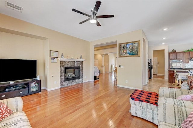 living area with visible vents, light wood finished floors, a premium fireplace, arched walkways, and ceiling fan