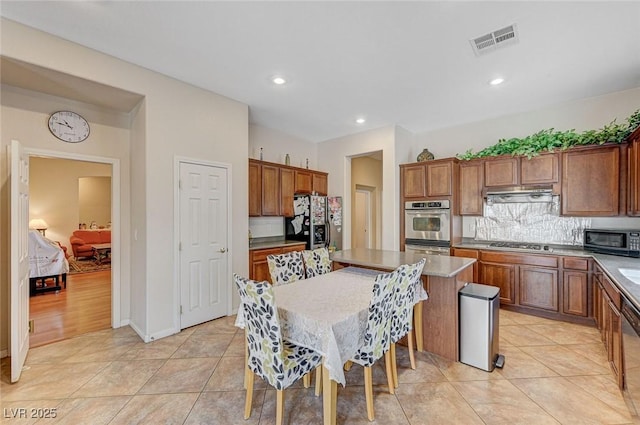 kitchen with visible vents, under cabinet range hood, light tile patterned floors, brown cabinetry, and stainless steel appliances