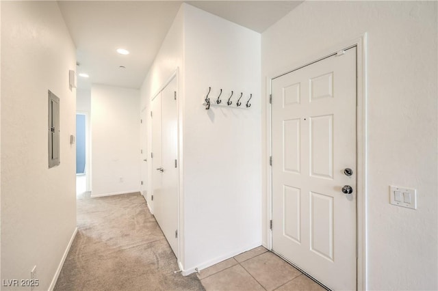 corridor with electric panel, baseboards, light carpet, and light tile patterned flooring