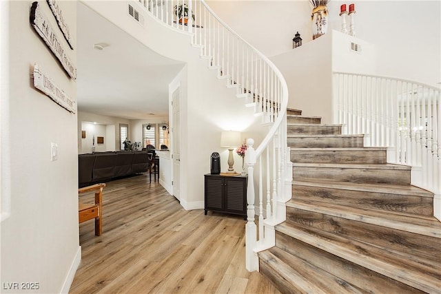 staircase with visible vents, a high ceiling, wood finished floors, and baseboards