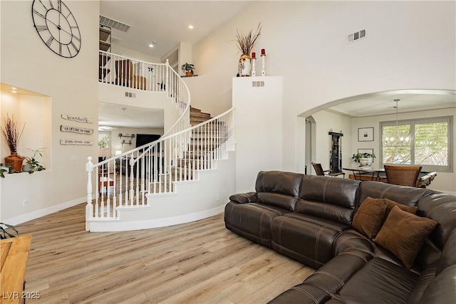 living area with visible vents, baseboards, stairs, a towering ceiling, and wood finished floors