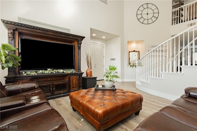 living area featuring stairway, baseboards, light wood-style floors, and a towering ceiling