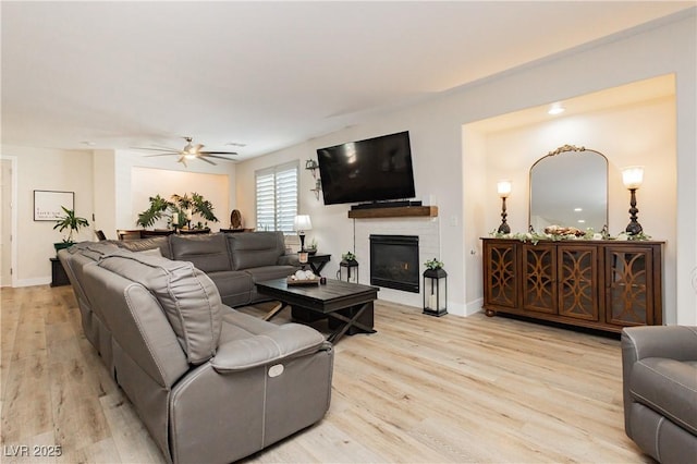 living area with a glass covered fireplace, baseboards, light wood finished floors, and ceiling fan